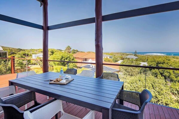 A covered outdoor seating area with a table and chairs, overlooking a coastal landscape.