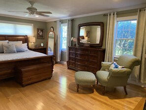 A bedroom with a large bed, a dresser, a chair, and a mirror.