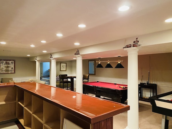 A pool table with a red felt surface, surrounded by white columns and a bar area with a wooden top. - BEAUTIFUL and PRIVATE OSTERVILLE HOME, LARGE GAME ROOM, AC,PARKING (Barnstable)