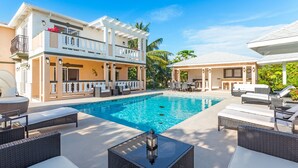 Un edificio de dos pisos con piscina, asientos al aire libre y un espacio cubierto con mesa y sillas.
