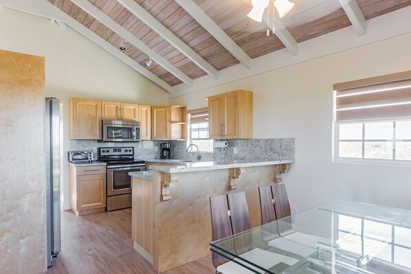 A modern kitchen with wooden cabinets, stainless steel appliances, and a glass dining table. - Sea La Vie - Beachside 2 Bedrooms Unit #4, with ocean views (Providenciales)