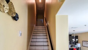 A staircase with a handrail, leading to a living area with a sofa, a red chair, and a coffee table. - 4BR Smart Luxe Condo w/ Pool View, Gated Community: close to Costco & Top Golf (McAllen)