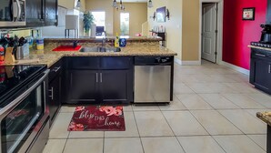A modern kitchen with dark cabinets, a granite countertop, stainless steel appliances, and a red doormat. - 4BR Smart Luxe Condo w/ Pool View, Gated Community: close to Costco & Top Golf (McAllen)