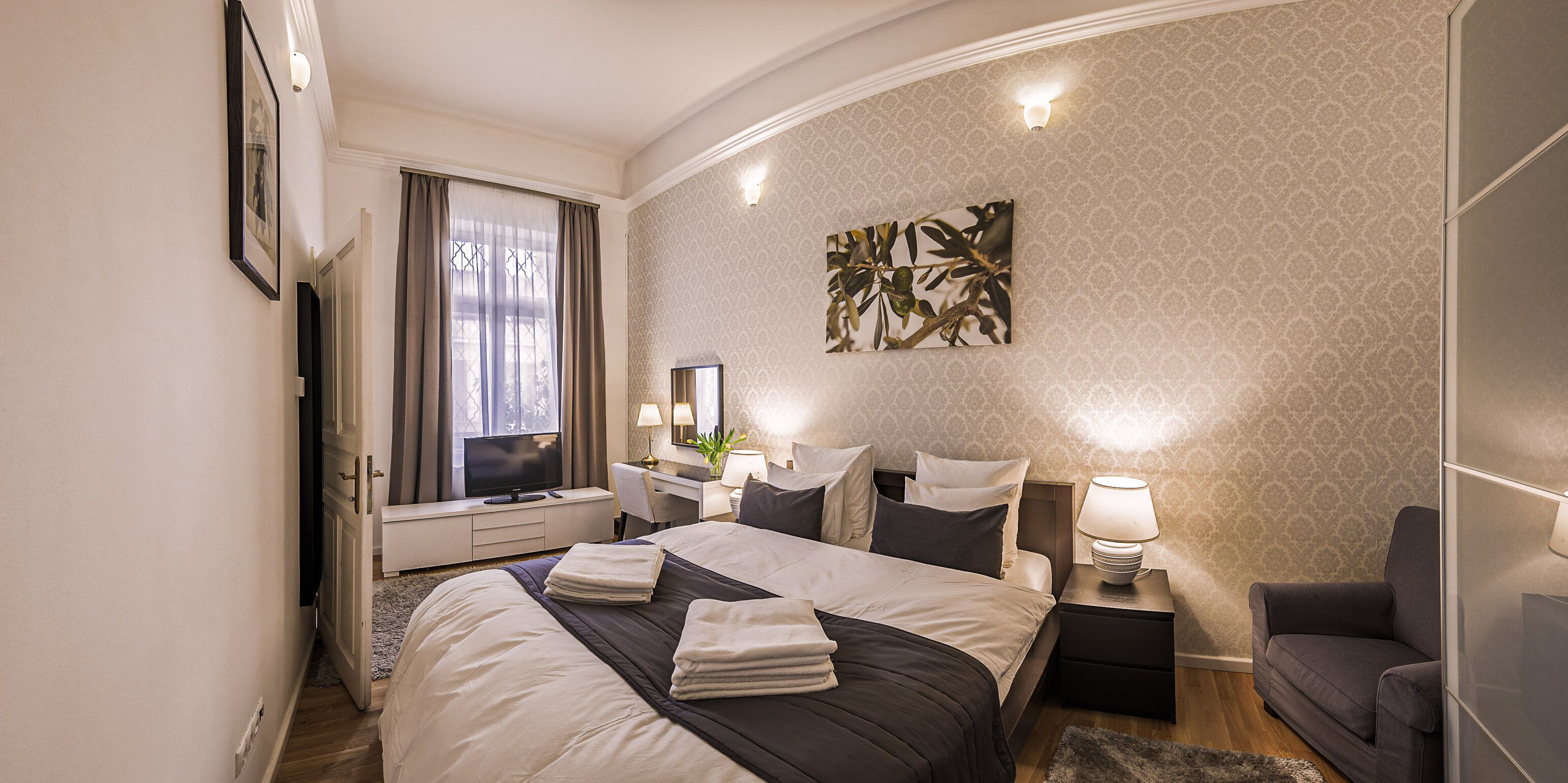 Une chambre d’hôtel comprenant un lit, des tables de chevet, un bureau, une chaise, une télévision et une fenêtre avec des rideaux.