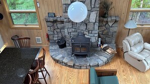A cozy cabin interior with a stone fireplace, wooden walls, a dining area with a granite table, and a seating area with a sofa and chairs. - Swim and Kayak at this freshwater location. Sleep 6+ on MDI near Acadia National (Seal Cove)