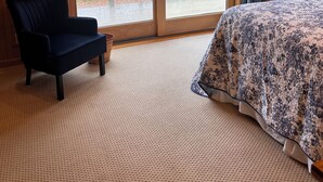 A bedroom with a large sliding glass door, a dark blue chair, a bed with a floral bedspread, and a wooden dresser. - Swim and Kayak at this freshwater location. Sleep 6+ on MDI near Acadia National (Seal Cove)