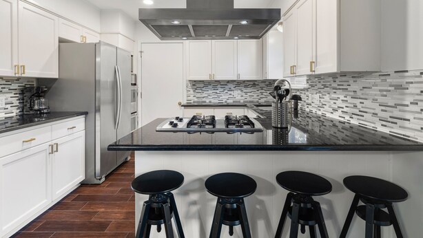 A modern kitchen with white cabinets, a stainless steel refrigerator, a gas stove, and a black countertop island with stools. - 2 Living Rooms, Lots of Big Beds! 3 king, 2 queen (Austin)