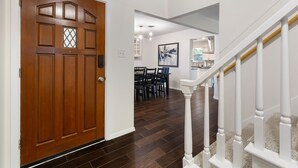 A hallway with a wooden door, a dining area with a table and chairs, and a staircase with white railings. - 2 Living Rooms, Lots of Big Beds! 3 king, 2 queen (Austin)
