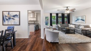 A modern living room with a grey sofa, a coffee table, and a dining area with a table and chairs. There is a ceiling fan and artwork on the walls. - 2 Living Rooms, Lots of Big Beds! 3 king, 2 queen (Austin)