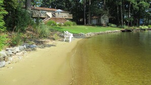 A lakeside property with a sandy beach, a wooden deck, and a house with a visible staircase.