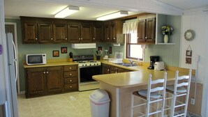 A kitchen with wooden cabinets, a microwave, stove, sink, and a trash can.