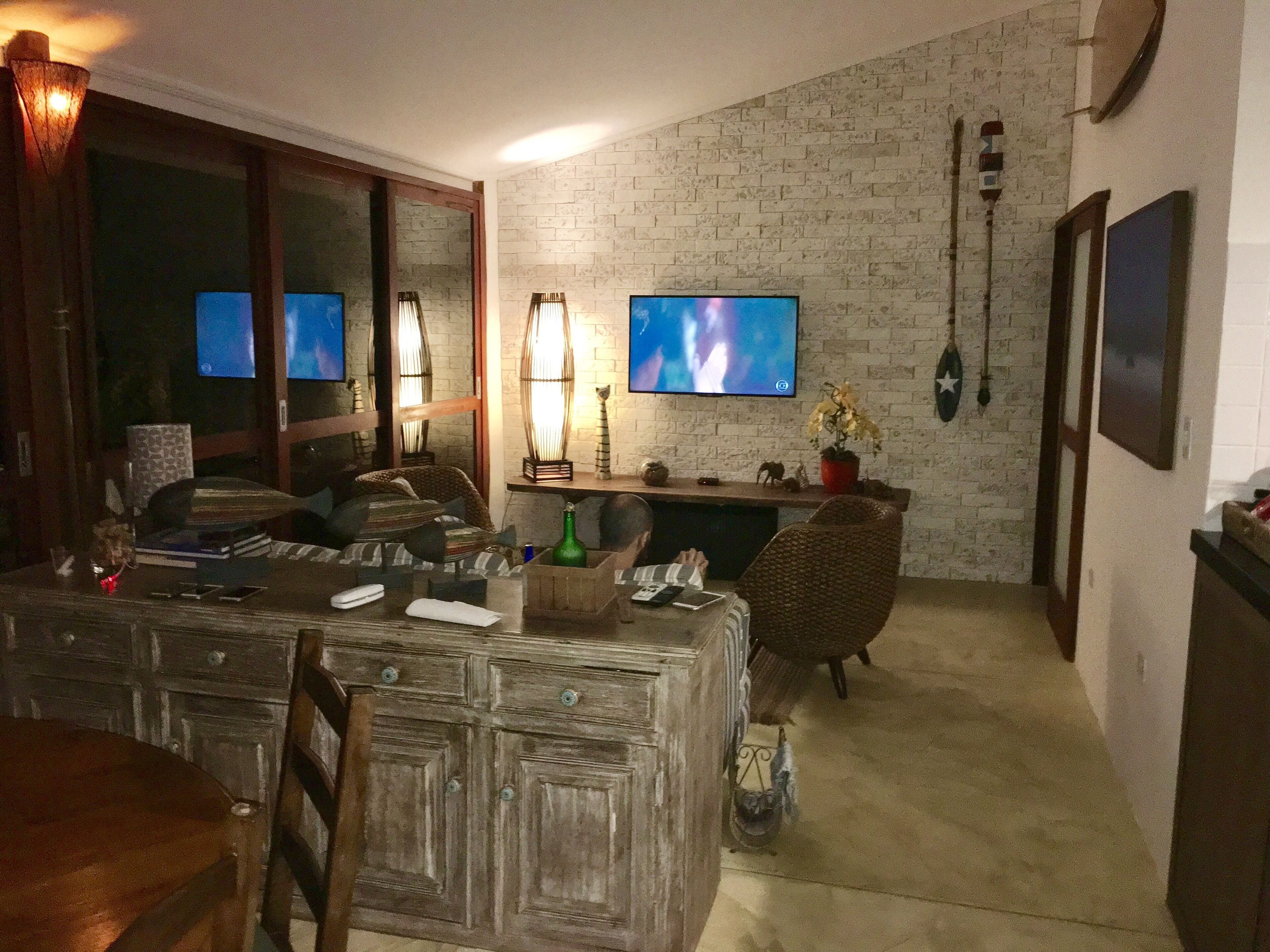 Ein gemütliches Wohnzimmer mit Backsteinwand, zwei Flachbildfernsehern, einem Holzesstisch und einer bequemen Sitzecke.