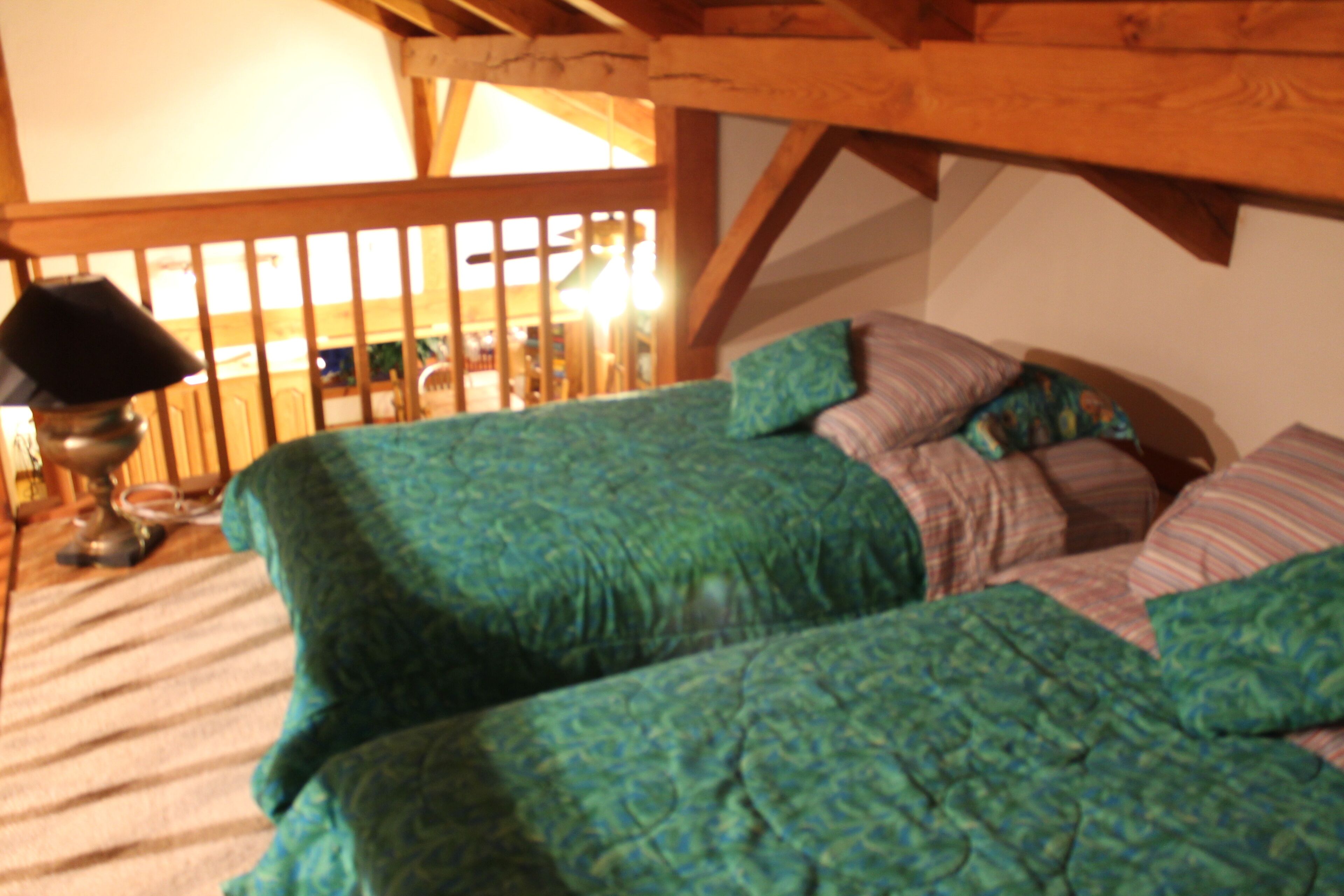 A room with two beds, wooden beams, a lamp, and a patterned bedspread.