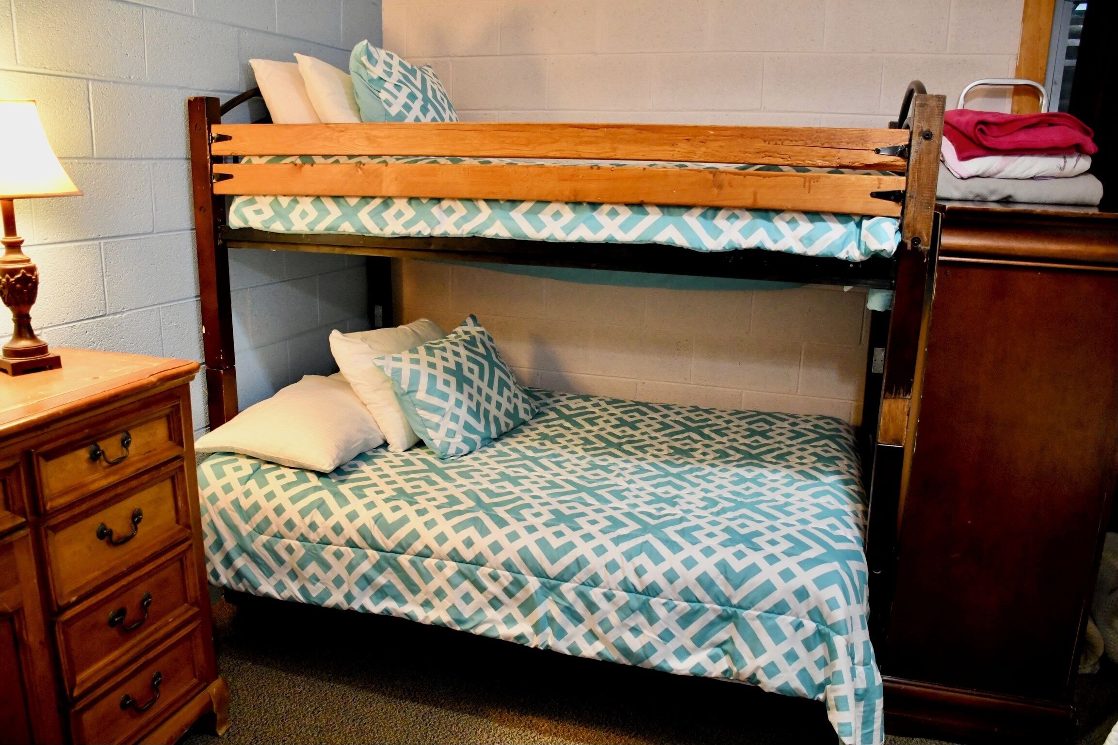 A bunk bed with patterned bedding, a wooden dresser, and a lamp.