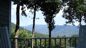 Ein Balkon mit zwei weißen Stühlen und einem kleinen Tisch, mit Blick auf eine gebirgige Landschaft.