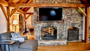 Ein gemütliches Wohnzimmer mit Kamin aus Stein, einem darüber befestigten Flachbildfernseher und einem bequemen grauen Sofa.