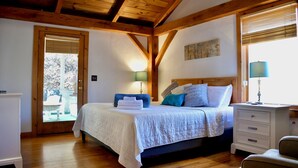 Ein Schlafzimmer mit Holzboden, einem Bett mit weißer Bettwäsche, einem Nachttisch, einem Sessel und einer Tür, die nach draußen führt.