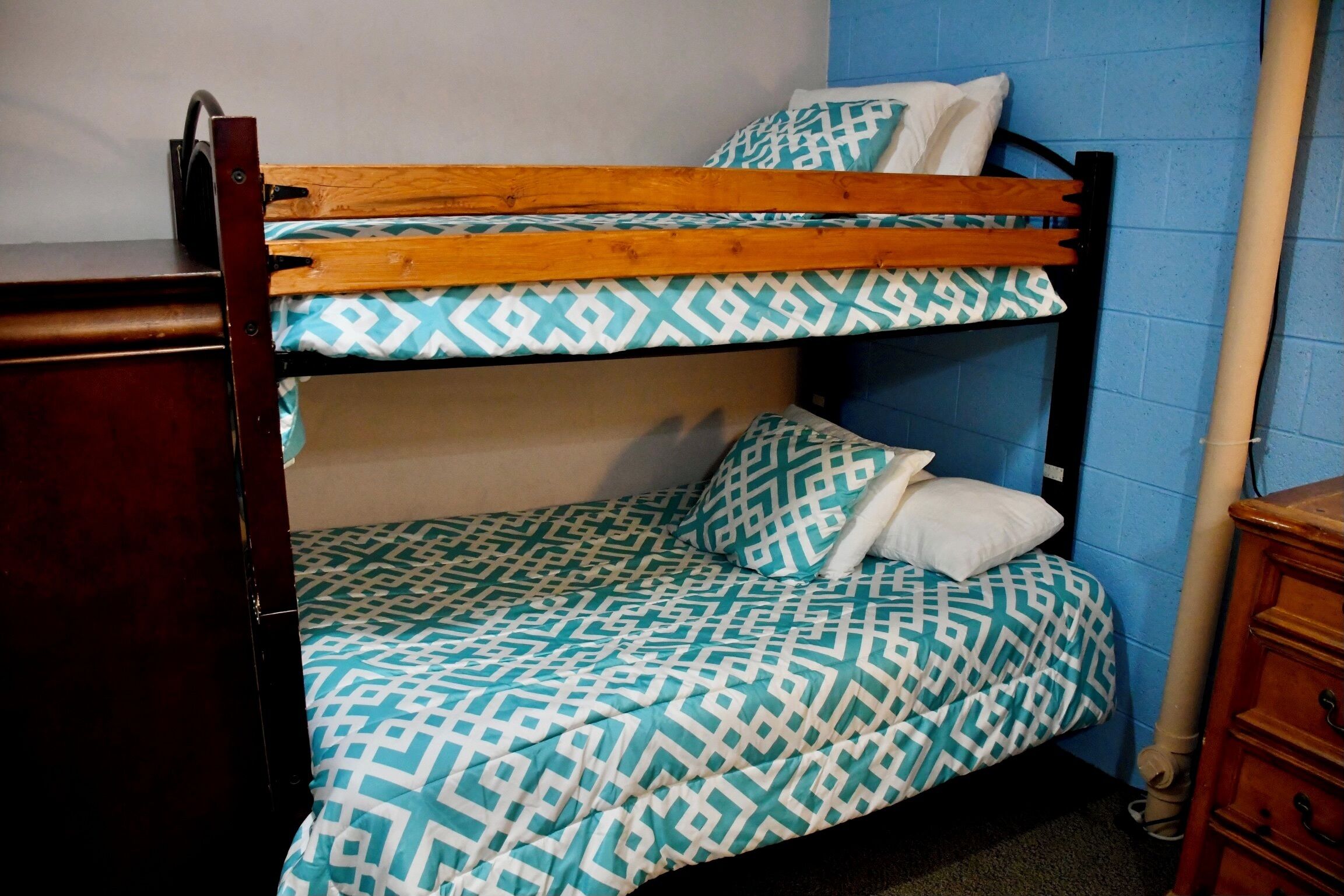 A bunk bed with patterned bedding, a wooden headboard, and a dresser.