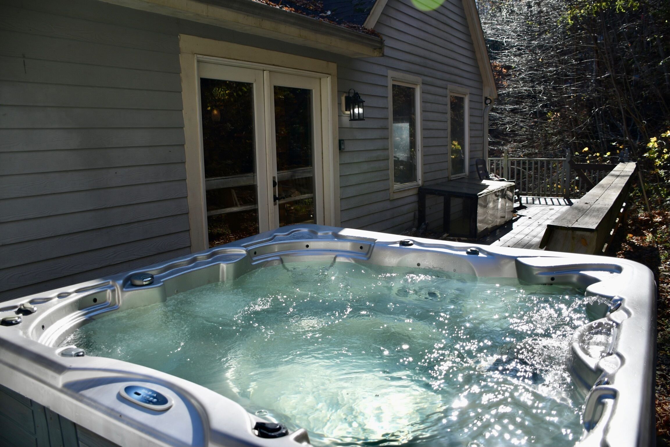 Un jacuzzi al aire libre frente a una casa con terraza y cerco de madera.