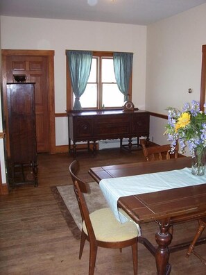 A dining room with a wooden table and chairs, a window with curtains, and a vase with flowers on the table. - Your next Vacation get away! (York Beach)