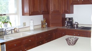 Una cocina con armarios de madera, encimera blanca, cafetera y pileta.