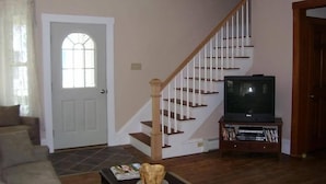 Una sala de estar con una escalera, un televisor y una puerta con ventana.