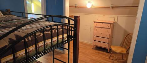 Ein Zimmer mit einem Etagenbett, einer Holzkommode, einem Stuhl und einer Tür zu einem anderen Raum.