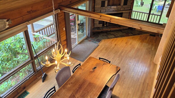 A wooden dining area with a chandelier, large windows, and a stone fireplace.