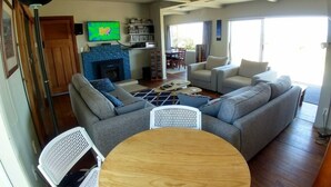 A modern living room with a grey sofa set, a wooden coffee table, and a TV mounted on the wall. - Magical Beach Kiwi Bach (Waitarere Beach)