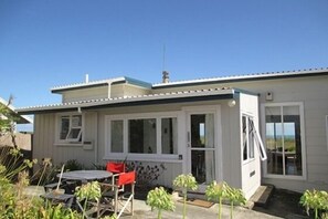 Una casa de un piso con un porche cubierto, una pequeña terraza y vista al océano.