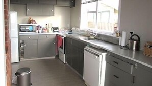 A compact kitchen with grey cabinets, a microwave, a sink, and a window with blinds. - Magical Beach Kiwi Bach (Waitarere Beach)