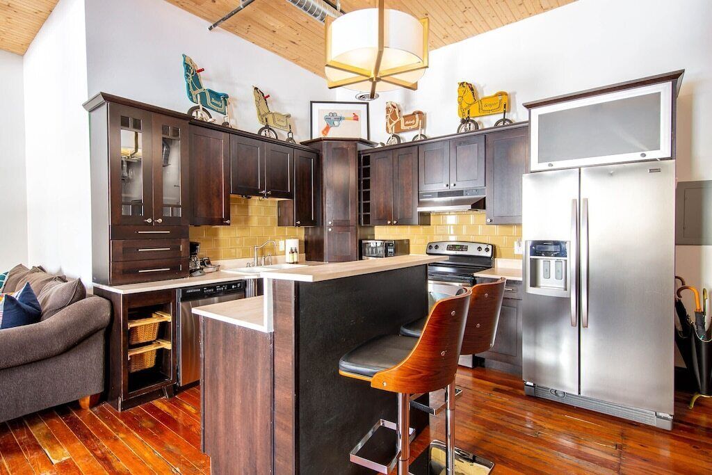 A modern kitchen with dark wooden cabinets, a stainless steel refrigerator, and a bar area with two stools.