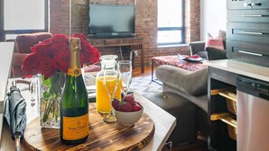 Une table en bois sur laquelle se trouvent une bouteille de champagne Veuve Clicquot, des verres de jus d’orange et un bol de fraises.