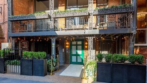 Un bâtiment à deux étages avec une porte verte, un espace extérieur aménagé pour s’asseoir et des plantes décoratives.