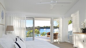 Une chambre avec un grand lit, une vue sur un plan d’eau et un balcon avec une chaise.