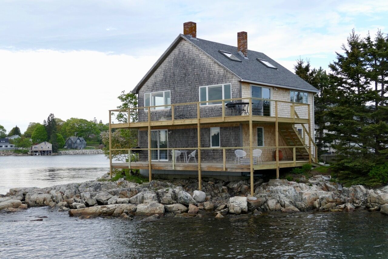 Una casa a due piani con un balcone, situata su una costa rocciosa con vista sull'acqua.