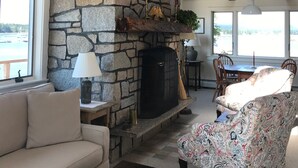 A cozy living room with a stone fireplace, a sofa, a patterned armchair, and a dining area with a table and chairs. - Upstairs level of two story home (Downstairs is a separate rental) in Bass Hbr. (Bass Harbor)