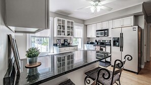 Une cuisine moderne avec des meubles blancs, un îlot central et un ventilateur de plafond.