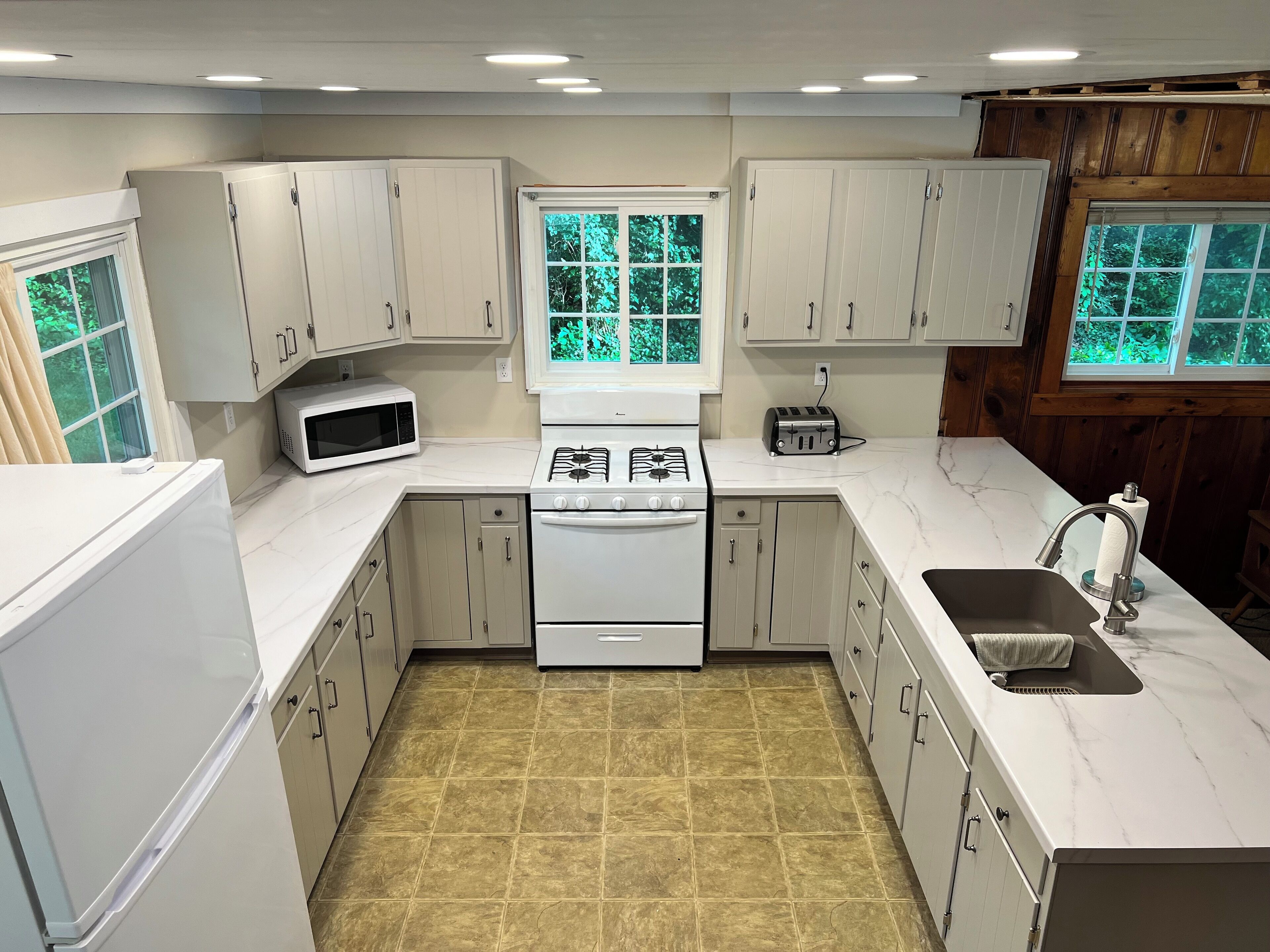 A modern kitchen with white cabinets, a stove, microwave, and a sink.