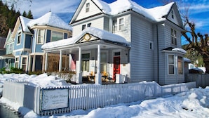 Ein großes, zweistöckiges Haus mit überdachter Veranda und umzäunter Garten, umgeben von Schnee.