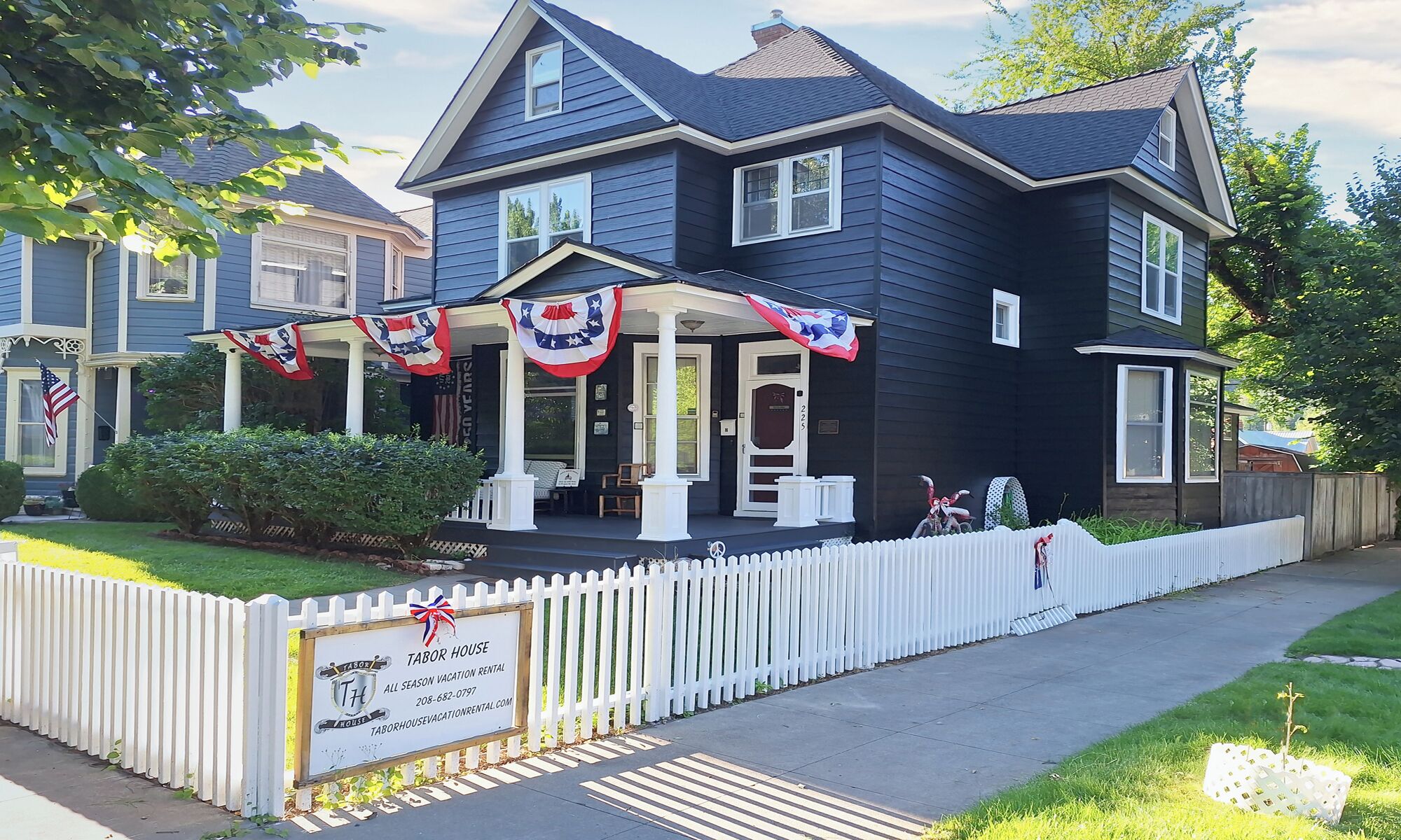 A two-story house with a porch, a picket fence, and a sign indicating it is a vacation rental.
