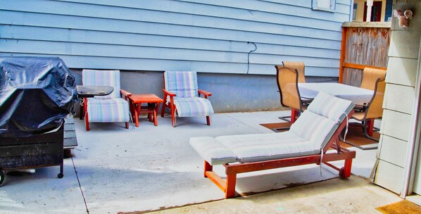 Une terrasse avec un barbecue, des chaises à rayures et un fauteuil de relaxation.