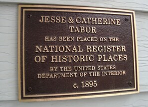 Une plaque fixée à un mur porte les noms de Jesse et Catherine Tabor et indique qu’ils figurent sur la liste nationale des lieux historiques. La date indiquée est 1895.