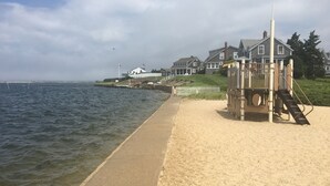 Een strand met een redershut, een zandpad en huizen op de achtergrond.