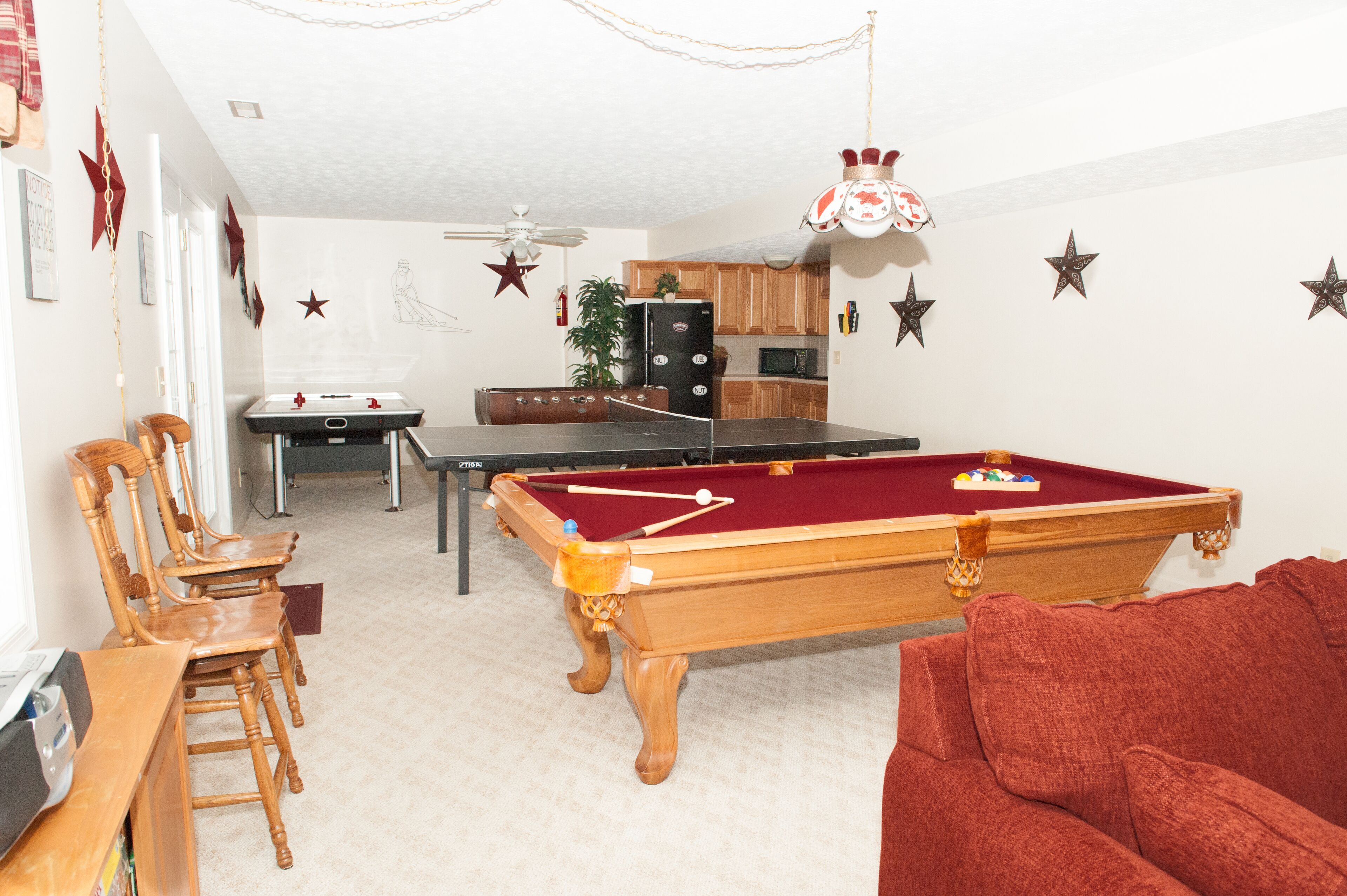 Een kamer met een pooltafel, houten stoelen, een rode bank en een keuken in de achtergrond.