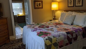 A bedroom with a large bed, a wooden dresser, a nightstand with a lamp, and framed pictures on the wall. - Downtown Bungalow! Dog Friendly -  WIFI!   (Brevard)
