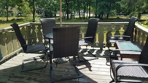 A covered outdoor seating area with wicker chairs and a table, surrounded by a wooden deck and a railing. - Jackson NH Peaceful, Country Cottage / Access to Fabulous Amenities (Bartlett)
