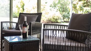 A wicker chair with a glass table, a bottle of wine, and a glass. - PET FRIENDLY COTTAGES - KELPIE COTTAGE - SELF CONTAINED COTTAGES (Worrolong, Mount Gambier)