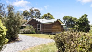 A wooden cabin with a gravel driveway, surrounded by dense vegetation and trees. - PET FRIENDLY COTTAGES - KELPIE COTTAGE - SELF CONTAINED COTTAGES (Worrolong, Mount Gambier)