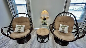 A room with three wicker chairs and a matching ottoman, each with a palm tree pillow. A table with a lamp and a small statue is in the center. - BEACH BLOCK, 100 steps to BOARDWALK and SAND, Sleeps 10 (Wildwood)